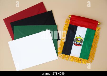 Kleine Flagge der VAE auf beigefarbenem Hintergrund mit bunten Umschlägen. Kopierbereich. Vorlage für Werbeanzeigen vortäuschen. Reisegutschein mit dem nationalen Symbol der Vereinigten Arabischen Emirate. Besuchen Sie Dubai Concept Stockfoto