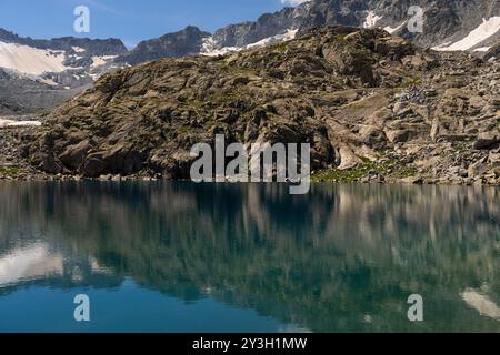 Klarer Bergsee mit seinen felsigen Klippen und schneebedeckten Gipfeln Stockfoto