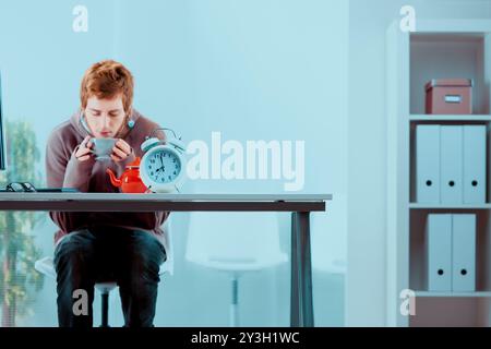 Junge Profis wärmt sich die Hände auf einer gemütlichen Tasse, genießen an einem kühlen Morgen im Büro ein heißes Getränk am Schreibtisch und finden eine Pause vom Arbeitsstress Stockfoto