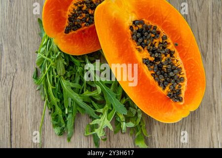 Papaya-Frucht und Rucola auf hellem Holzhintergrund. Scheiben süßer Papayas auf hölzernem Hintergrund, halbierte Papayas, Kopierraum für Text Stockfoto