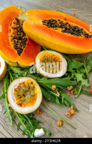 Papaya-Frucht, Passionsfrucht, Rucola und Müsli auf hellem hölzernem Hintergrund. Scheiben süßer Papaya, Maracuja, grüner Rucola umgeben von Granola fla Stockfoto