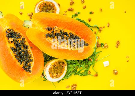 Papaya, Passionsfrucht, Rucola und Müsli auf gelbem Hintergrund. Scheiben von süßer Papaya, Passionsfrucht, Rucola umgeben von Granola Flocken auf Gelb Stockfoto