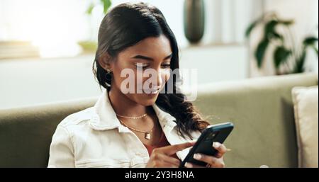 Gesicht, Telefon und Suche mit indischer Frau auf Sofa im Wohnzimmer des Hauses für Internet-Browsing. App, Lächeln und soziale Medien mit glücklicher Person Stockfoto