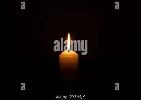 Eine einzelne brennende Kerzenflamme oder Licht, das auf einer großen weißen Kerze leuchtet, wird auf schwarzem oder dunklem Hintergrund auf dem Tisch in der Kirche für Weihnachten, Beerdigung isoliert Stockfoto
