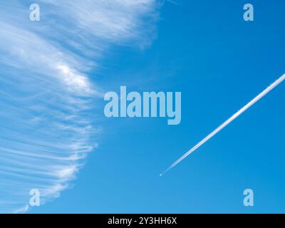 Wirbelnde Zirruswolken (Stutenschwänze) vor klarem blauem Himmel mit Jetflugzeug-Kondensstreifen/Dampfpfad Stockfoto