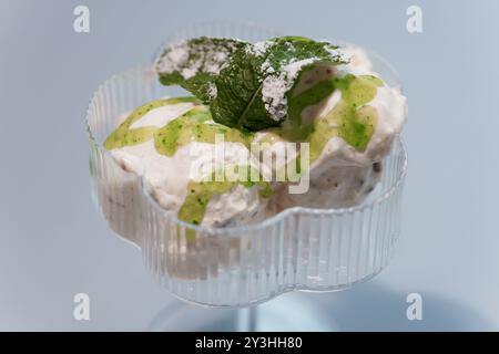 Exquisites cremiges Dessert mit Mint Garnish in eleganter Glasschale vor weichem blauem Hintergrund. Stockfoto