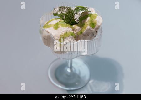 Elegante Dessertpräsentation mit Mint Garnish in einer Vintage-Glasschale vor weichem blauem Hintergrund. Stockfoto