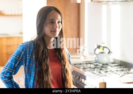 Zu Hause, lächelnde junge asiatische Frau, die in der Küche in der Nähe des Herds steht und ein lässiges kariertes Hemd trägt Stockfoto