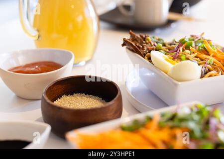 Zu Hause, Nahaufnahme der asiatischen Küche mit Salat, Sesamsamen und Orangensaft auf dem Tisch Stockfoto