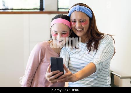 Zu Hause machen Selfie, asiatische Mutter und Tochter lächeln mit Gesichtsmasken im Badezimmer Stockfoto