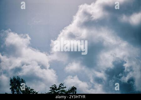 Tauchen Sie ein in die Gelassenheit dieses Stockbildes, das weiche Kumuluswolken zeigt, die in einem sanften blauen Himmel schweben. Sonnenlicht filtert durch das f Stockfoto