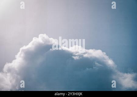 Genießen Sie die Ruhe dieses Stockbildes, das weiche Kumuluswolken zeigt, die in einem ruhigen blauen Himmel schweben. Sonnenlicht dringt sanft in das flauschige Format ein Stockfoto