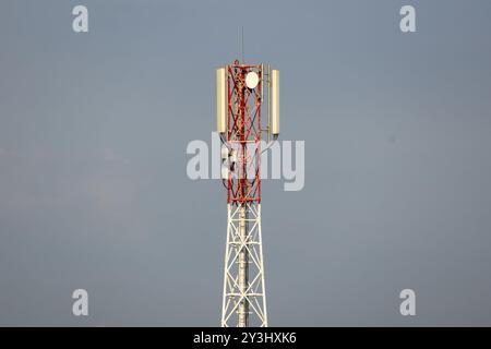 Direktionales Antennenarray auf einem rot-weißen Kommunikationsturm gegen den Himmel. Mobilfunknetzwerkinfrastruktur für drahtlose Kommunikation. Ein Symbol von Stockfoto