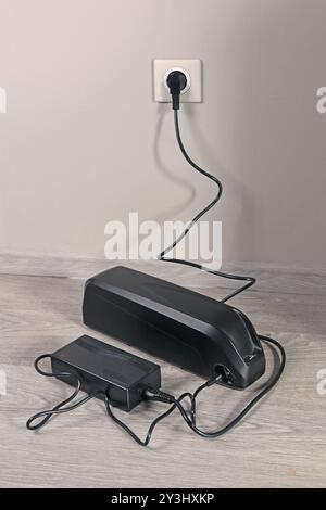 Laden der Fahrradbatterie über das Stromnetz im Haus. Steckdose im Zimmer mit eingeschaltetem Stecker. Umweltfreundlicher Transport. Stockfoto