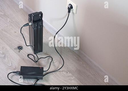 Laden der Fahrradbatterie über das Stromnetz im Haus. Steckdose im Zimmer mit eingeschaltetem Stecker. Umweltfreundlicher Transport. Stockfoto