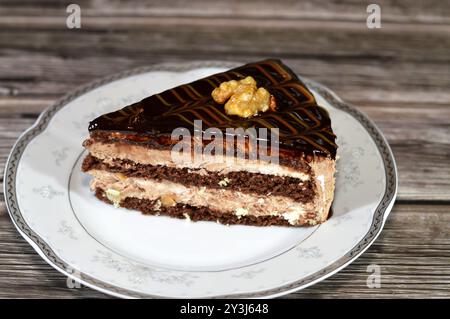 Dreieckiges Schokoladenkuchenstück gefüllt und garniert mit Walnuss, Schichten Schokoladenpaste Creme und Stücken, mit Schichten Schlagsahne, serviert Stockfoto