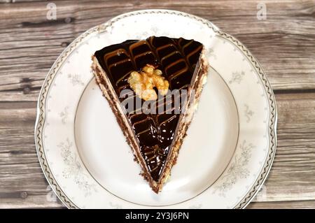 Dreieckiges Schokoladenkuchenstück gefüllt und garniert mit Walnuss, Schichten Schokoladenpaste Creme und Stücken, mit Schichten Schlagsahne, serviert Stockfoto