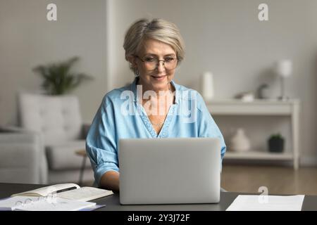 Zielgerichtete, reife Frau, die am Schreibtisch sitzt und einen Laptop benutzt Stockfoto