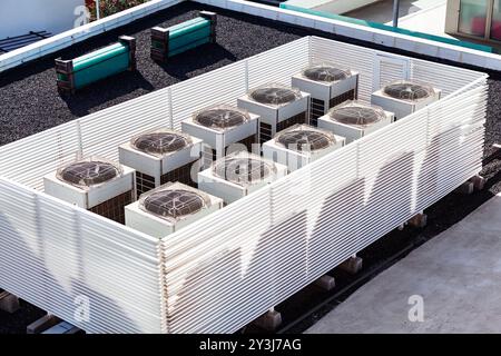 Eine Reihe von Klimaanlagen befindet sich auf einem Dach. Mehrere Klimaanlagen auf dem Dach. Weiße Ventilatoren auf dem Dach drehen sich, wenn sie Luft ablassen Stockfoto