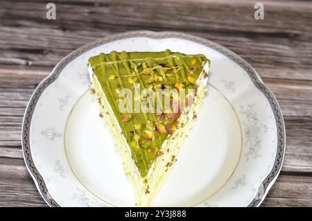 Dreieckiges Stück Pistazienkuchen gefüllt und belegt mit Schichten Pistazienpaste Creme und Stückchen, mit Kuchenschichten, serviert auf einem Teller und ich Stockfoto