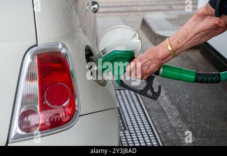 Die Hand einer Frau, die eine grüne Kraftstoffdüse hält, steckt sie in den Benzintank eines weißen Autos und betankt ihr Auto. Stockfoto