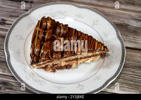 Ein dreieckiges, schwammiges Kuchenstück aus Schokolade, gefüllt mit Schichten Schokoladenpaste Creme und Kugelstücken, mit Kuchenschichten, serviert auf einer Platte Stockfoto