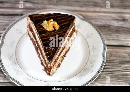 Dreieckiges Schokoladenkuchenstück gefüllt und garniert mit Walnuss, Schichten Schokoladenpaste Creme und Stücken, mit Schichten Schlagsahne, serviert Stockfoto