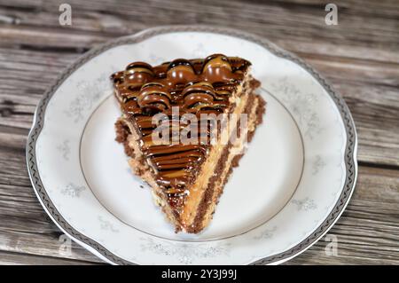 Ein dreieckiges, schwammiges Kuchenstück aus Schokolade, gefüllt mit Schichten Schokoladenpaste Creme und Kugelstücken, mit Kuchenschichten, serviert auf einer Platte Stockfoto