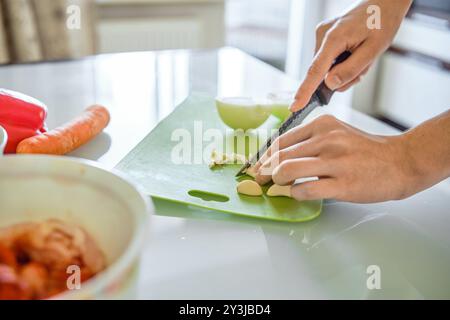Unbekannte Frau zerkleinert gekonnt Knoblauch und Zwiebeln auf einem leuchtend grünen Schneidebrett Stockfoto