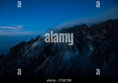 Nächtlicher Blick auf schwefelhaltigen Rauch vom Vulkan Merapi, der in schwarzer Silhouette aus den Felsen kommt Stockfoto