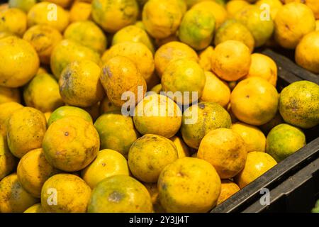 Eine Nahaufnahme eines Haufens von gelben und grünen Zitrusfrüchten, möglicherweise Orangen oder Mandarinen, in einem Marktumfeld. Die Früchte haben ein wenig Stockfoto