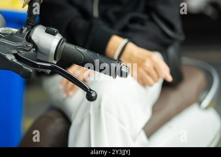 Nahaufnahme eines Motorradlenkergriffs mit der Hand einer Person in der Nähe, die Details des Griffs und der Kleidung der Person in einem verschwommenen B zeigt Stockfoto