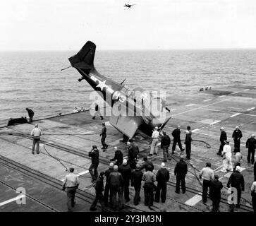 Ein General Motors FM-2 Wildcat-Kampfflugzeug der US Navy stürzte nach einem Absturz an Bord des Trainingsträgers USS Sable (IX-81) während des Pilotentrainings in den Großen Seen im Mai 1945 um. Eine weitere FM-2 fliegt in der Mitte vorbei - Foto der US Navy Stockfoto