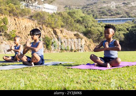 Yoga auf Matten üben, multirassische Jungen, die während der Schulaktivität im Freien meditieren Stockfoto