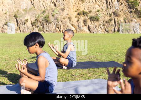 Yoga praktizieren, multirassische Jungs sitzen draußen auf Matten in der Schule Stockfoto