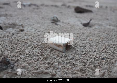 Ein entsorgtes und verwittertes elektrisches Bauteil liegt an einem Sandstrand und trägt weiter zur Verschmutzung und zum Abfall an der Küste bei Stockfoto