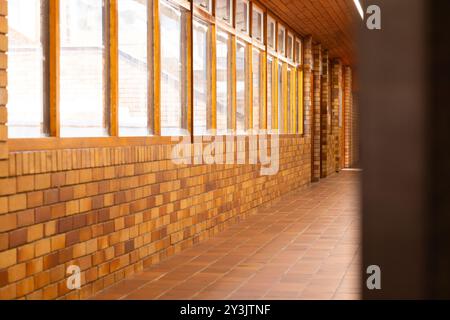 Leerer Schulflur mit Ziegelwänden und großen Fenstern, hell und sauber Stockfoto