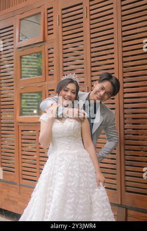 Ein Paar Männer und Frauen in eleganten Posen stehen lachend, mit Männerhänden, die sich hinter dem Körper der Frau umarmen, während sie ihre Augen mit einem Beau schließen Stockfoto