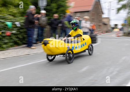 Zschaiten, Deutschland. September 2024. Ein Mann reitet eine Banane im Seifenboxen-Rennen in Zschaiten, Sachsen, um die beste Zeit. Die kleine Gemeinde bei Riesa feiert am 13-15. September 2024 ihr 700-jähriges Bestehen. Darlegung: Daniel Wagner/dpa/Alamy Live News Stockfoto