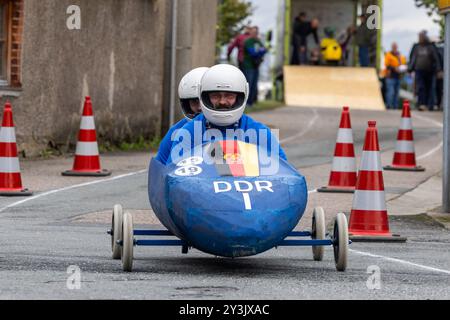 Zschaiten, Deutschland. September 2024. Zwei Männer sitzen in einer als DDR 1-Bob gestalteten Seifenbox. Die Teilnehmer fahren mit ihren bizarren Kostümen und Fahrzeugen um die beste Zeit. Darlegung: Daniel Wagner/dpa/Alamy Live News Stockfoto