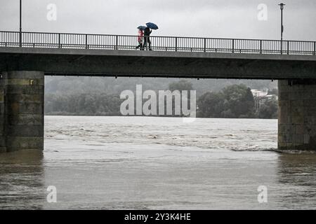 Passau, Deutschland. September 2024. Passanten mit Sonnenschirmen auf einer Brücke über das überflutete Inn. Auch wenn der meiste Teil des Wochenendregens in Bayern bereits gefallen ist, werden sich die Niederschläge auf den Flüssen erst Stunden oder Tage später bemerkbar machen. In Passau, wo drei Flüsse aufeinander treffen, sollte nach Angaben der Stadt in den Abendstunden mit den ersten Schließungen in der Altstadt gerechnet werden. Quelle: Armin Weigel/dpa/Alamy Live News Stockfoto