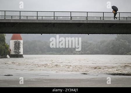 Passau, Deutschland. September 2024. Passanten mit Sonnenschirmen auf einer Brücke über das überflutete Inn. Auch wenn der meiste Teil des Wochenendregens in Bayern bereits gefallen ist, werden sich die Niederschläge auf den Flüssen erst Stunden oder Tage später bemerkbar machen. In Passau, wo drei Flüsse aufeinander treffen, sollte nach Angaben der Stadt in den Abendstunden mit den ersten Schließungen in der Altstadt gerechnet werden. Quelle: Armin Weigel/dpa/Alamy Live News Stockfoto