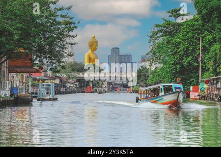 Blick auf die große Buddha-Statue in Bangkok, Thailand (Wat Pak Nam Phasi Charoen) vom Kanal aus mit Holzhäusern und Langschwanzbooten Stockfoto