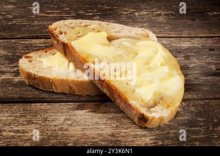 Studio-Aufnahme von Butter, die auf Sauerteigbrotscheiben schmilzt, die auf einem dunklen Holzhintergrund ruhen - John Gollop Stockfoto