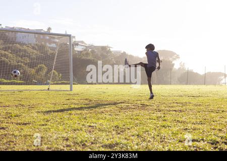 Draußen, Fußball in Richtung Tor, Junge spielt im Morgenlicht auf dem Schulfeld Stockfoto