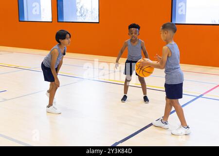 Basketball in der Schule spielen, drei multirassische Jungen trainieren in Sportbekleidung Stockfoto