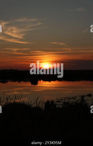 Ein dramatischer Sonnenuntergang spiegelt sich in einem Sumpfgebiet auf der deutschen Insel Föhr. Stockfoto