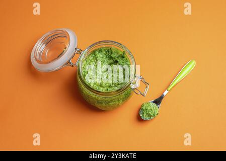 Öffnen Sie den Behälter mit grüner Pesto-Sauce auf einem nahtlosen orangen Hintergrund. Hausgemachtes Pesto aus Basilikum, Käse, Knoblauch und Öl. Italienische Nudelsauce Stockfoto