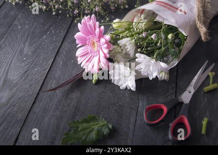 Oben sehen Sie ein Bild über die Aktivität der Blumenverpackung, mit einem Strauß von Chrysanthemenblumen in Zeitung, umgeben von einer Schere und links Stockfoto