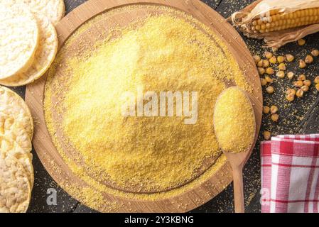 High Angle View Bild mit einem Stapel von Mais Mehl auf eine runde Holzplatte mit Maiskolben, Körner und Gepuffter mais Kuchen umgeben, auf einem schwarzen Holztisch Stockfoto